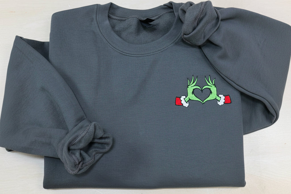 Show your Grinch Love with this Embroidered Sweatshirt. Featuring The Grinch hands shaped like a heart.