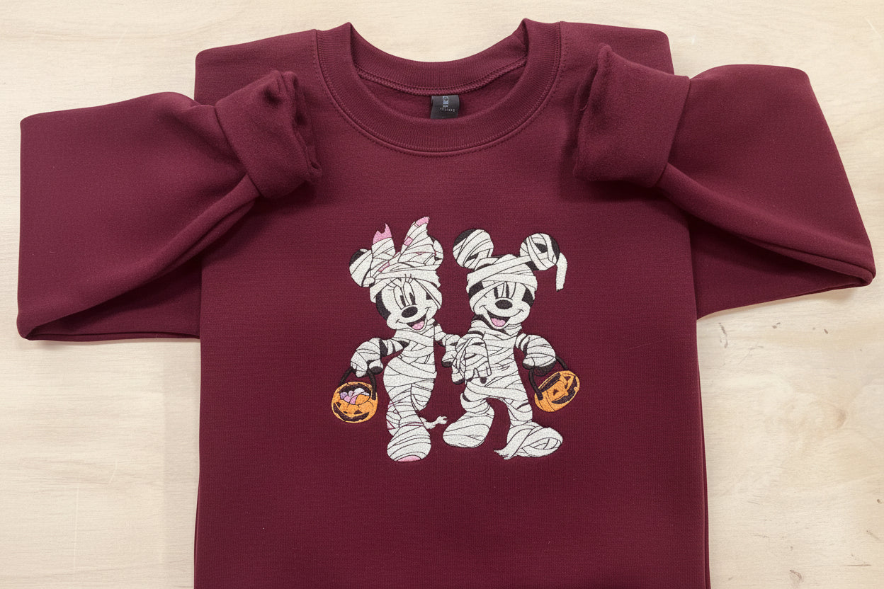 Halloween fun with our cozy embroidered sweatshirt featuring “Mickey & Minnie” all dressed up in their mummy costumes. Trick or Treat!