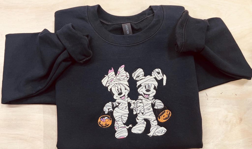 Halloween fun with our cozy embroidered sweatshirt featuring “Mickey & Minnie” all dressed up in their mummy costumes. Trick or Treat!