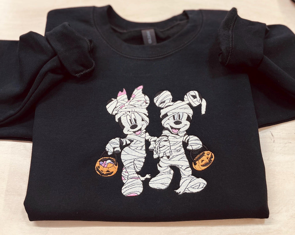Halloween fun with our cozy embroidered sweatshirt featuring “Mickey & Minnie” all dressed up in their mummy costumes. Trick or Treat!