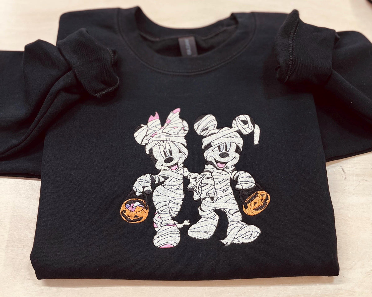 Halloween fun with our cozy embroidered sweatshirt featuring “Mickey & Minnie” all dressed up in their mummy costumes. Trick or Treat!