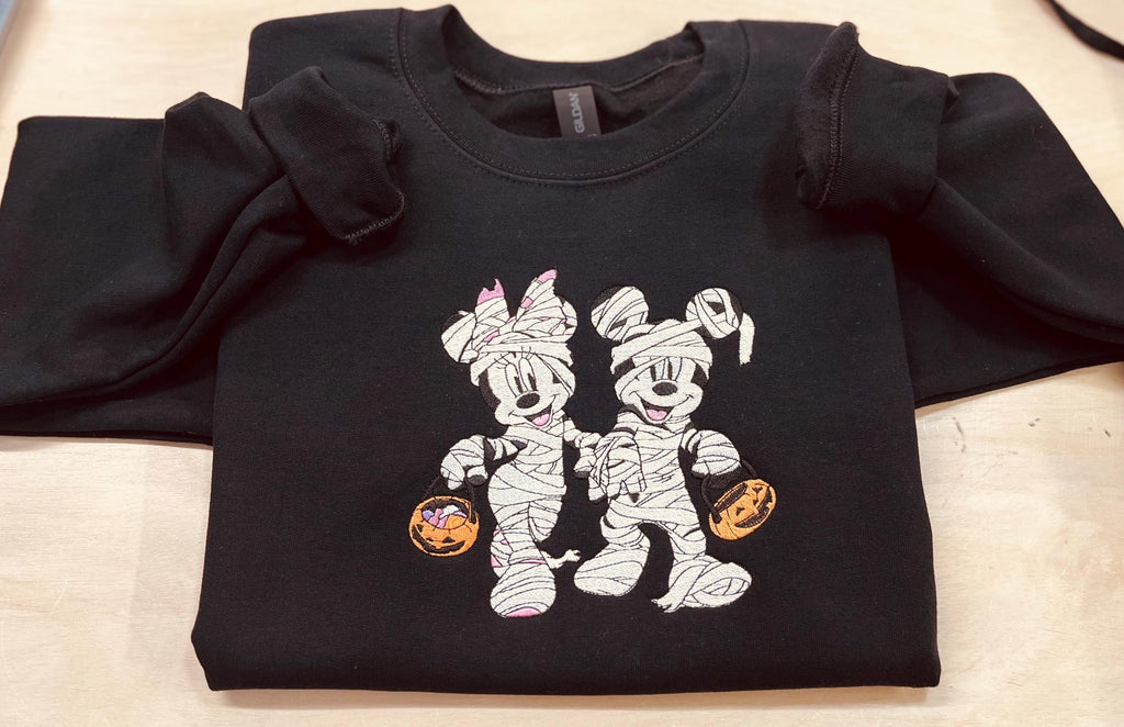 Halloween fun with our cozy embroidered sweatshirt featuring “Mickey & Minnie” all dressed up in their mummy costumes. Trick or Treat!
