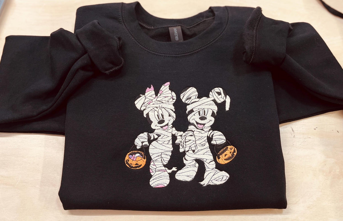 Halloween fun with our cozy embroidered sweatshirt featuring “Mickey & Minnie” all dressed up in their mummy costumes. Trick or Treat!