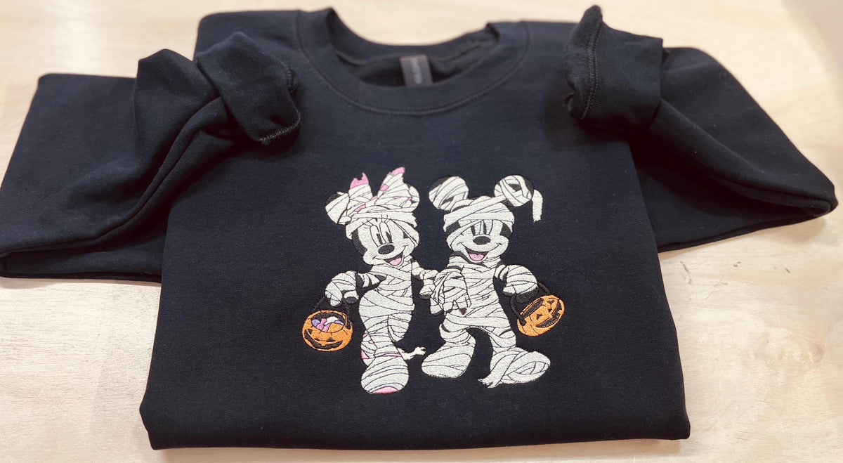 Halloween fun with our cozy embroidered sweatshirt featuring “Mickey & Minnie” all dressed up in their mummy costumes. Trick or Treat!
