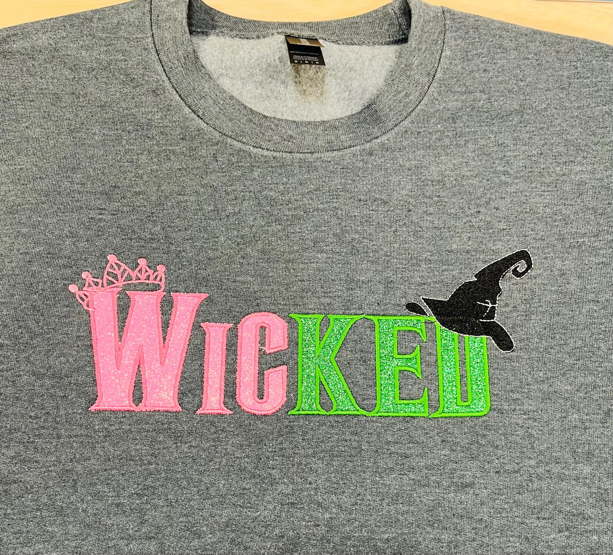 WICKED! This sparkly, embroidered wicked sweatshirt is perfect for Wicked fans. Includes a sleeve embellishment of a Green Broom/Pink Wand